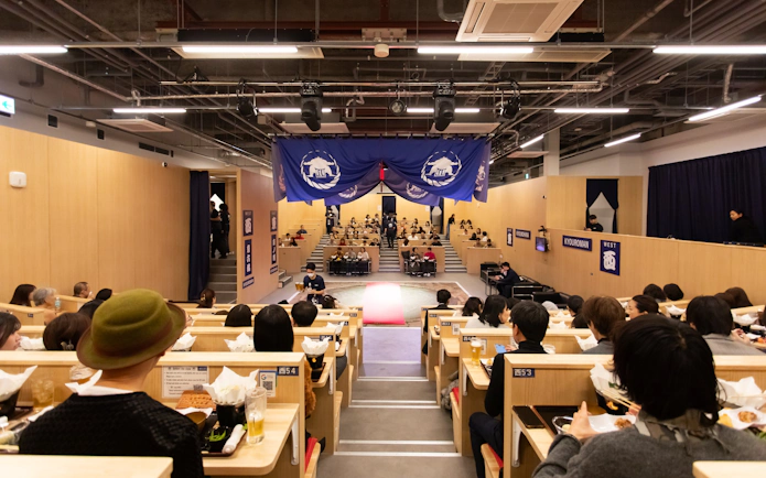 Kyoto sumo show audience dining on chicken hot pot in theater setting.