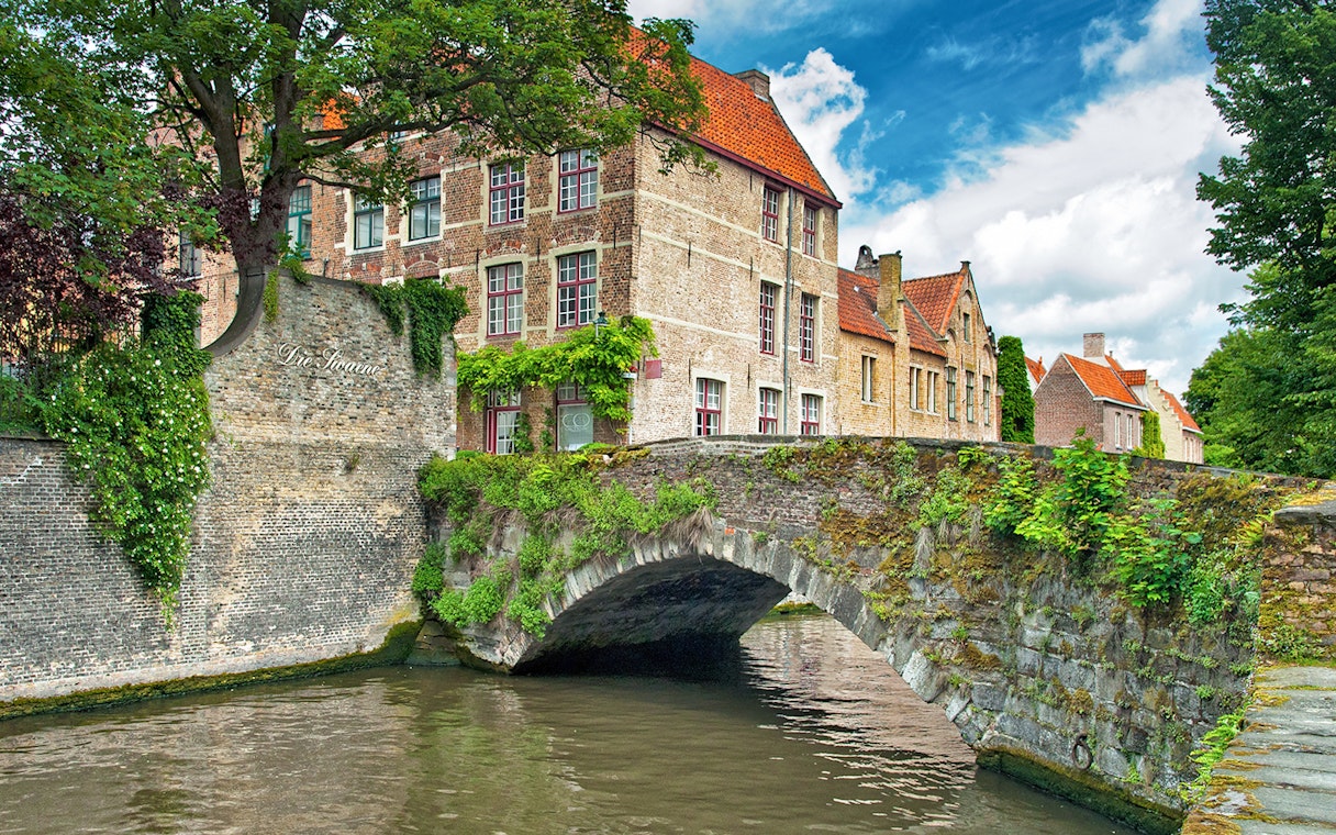 Historic stone bridge and canal in Bruges, Belgium, with traditional brick buildings.