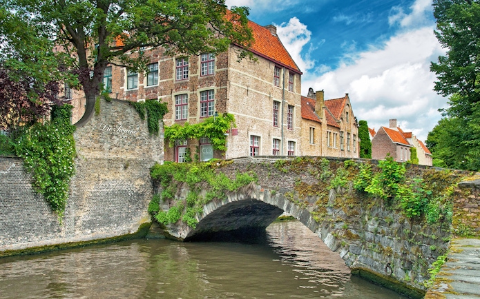 Historic stone bridge and canal in Bruges, Belgium, with traditional brick buildings.