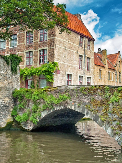 Historic stone bridge and canal in Bruges, Belgium, with traditional brick buildings.