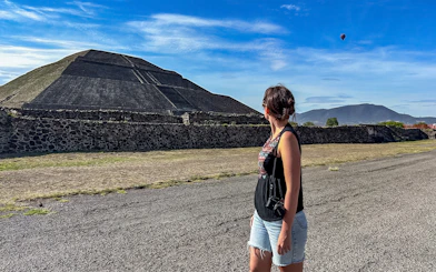 Woman observing Pyramid of the Sun at Teotihuacan with a hot air balloon in the sky.