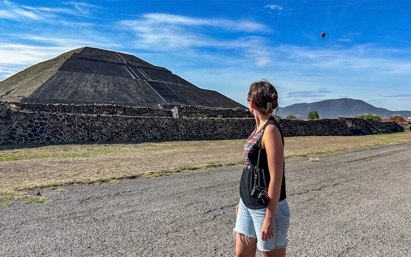 Woman observing Pyramid of the Sun at Teotihuacan with a hot air balloon in the sky.