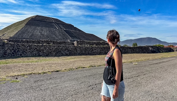 Woman observing Pyramid of the Sun at Teotihuacan with a hot air balloon in the sky.
