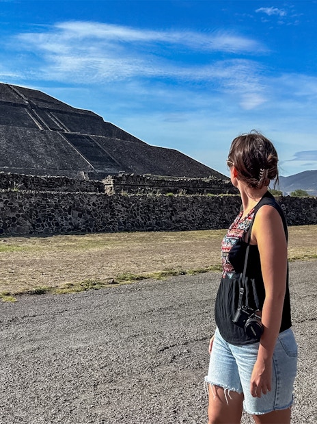 Woman observing Pyramid of the Sun at Teotihuacan with a hot air balloon in the sky.