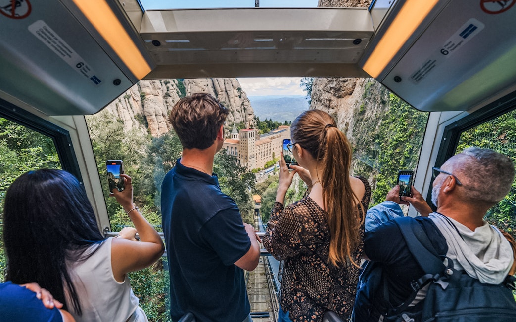 Tourists photographing Montserrat Monastery from train window.