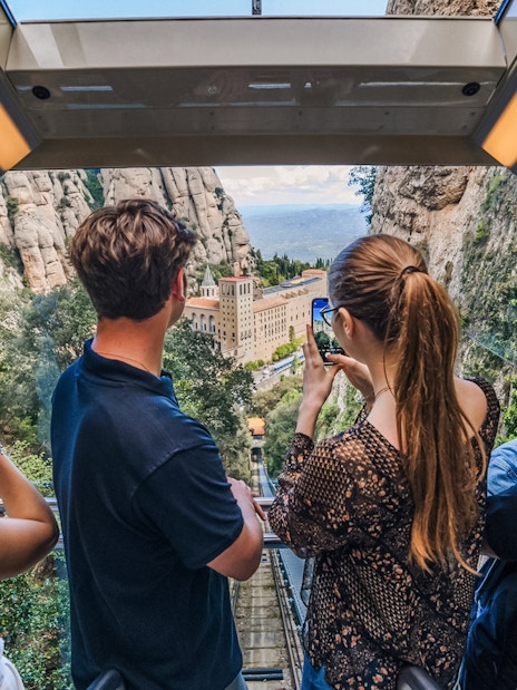 Tourists photographing Montserrat Monastery from train window.