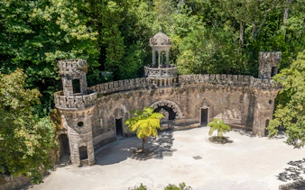 Gothic-style entrance with towers at Quinta da Regaleira, Sintra, surrounded by lush greenery.