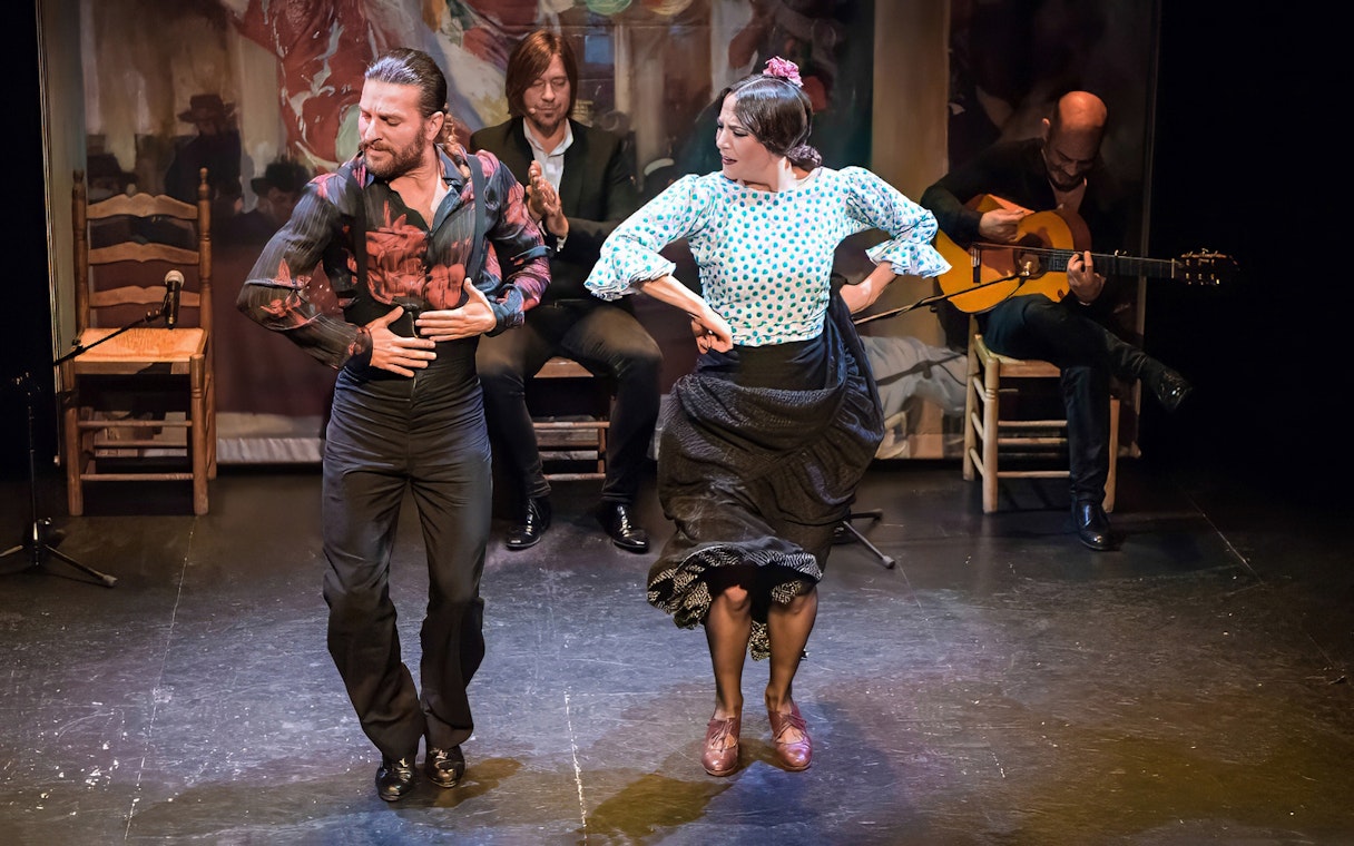 Flamenco dancers performing at Teatro Flamenco Triana with musicians in the background.