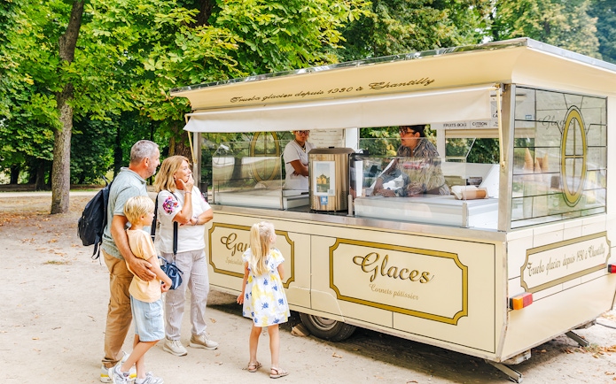 Family buying ice cream at a vintage cart in Chateau of Chantilly gardens.