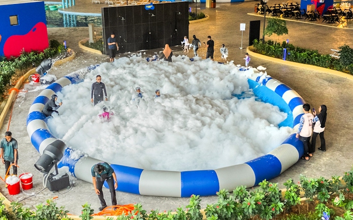 Kids and adults enjoying foam in a splash zone at an indoor water park.