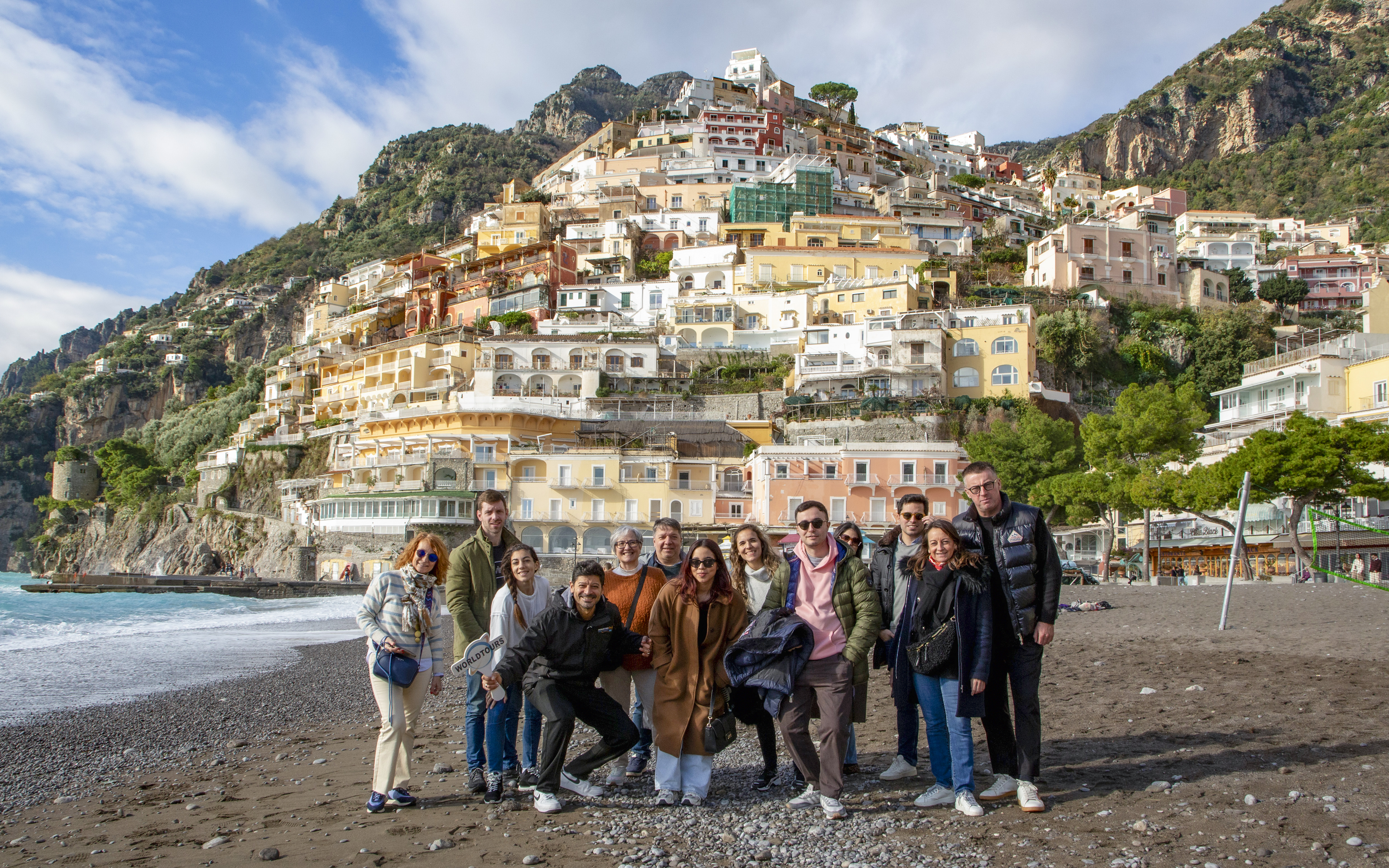 Tourists on the beach in Positano with colorful hillside buildings in the background.
