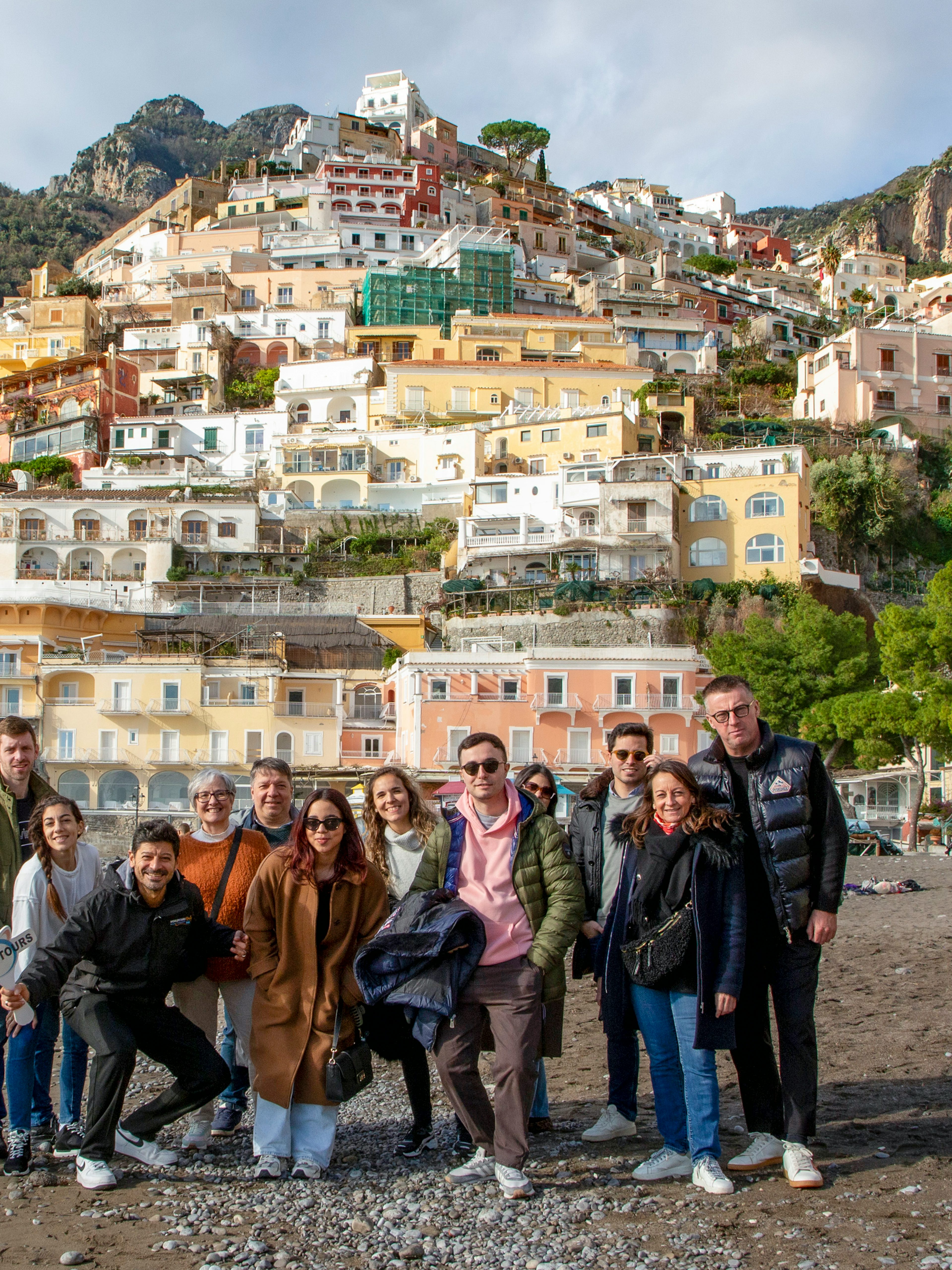Tourists on the beach in Positano with colorful hillside buildings in the background.