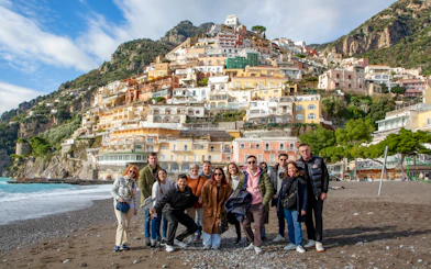 Tourists on the beach in Positano with colorful hillside buildings in the background.