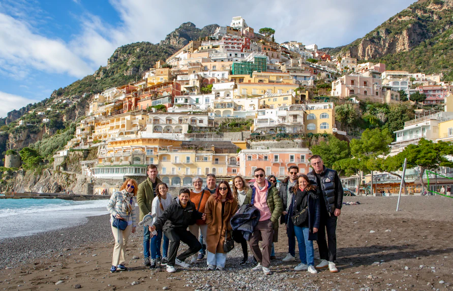 Tourists on the beach in Positano with colorful hillside buildings in the background.