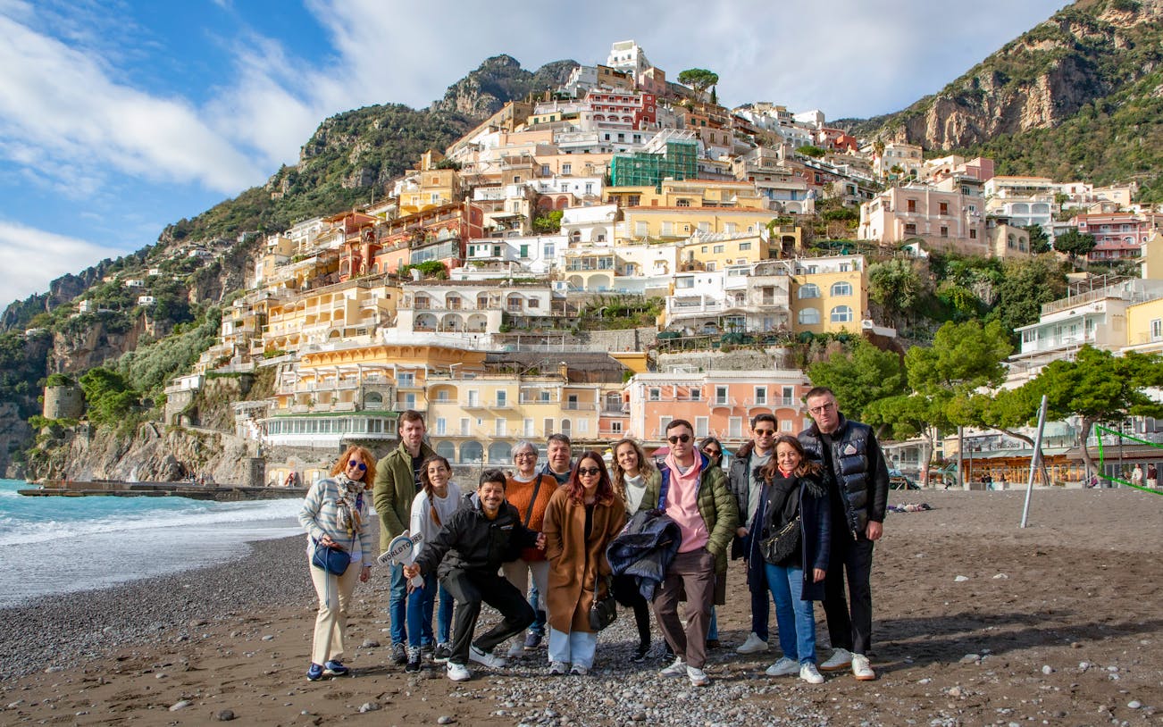 Tourists on the beach in Positano with colorful hillside buildings in the background.