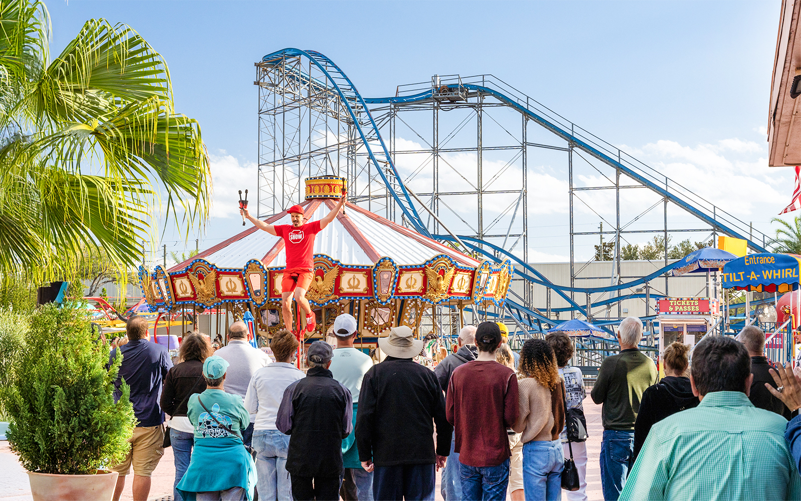 Performer entertaining crowd near carousel and roller coaster at Old Town, Orlando.