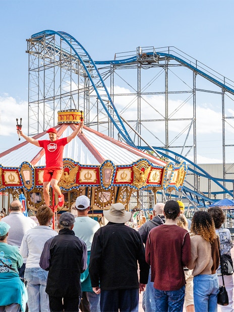 Performer entertaining crowd near carousel and roller coaster at Old Town, Orlando.