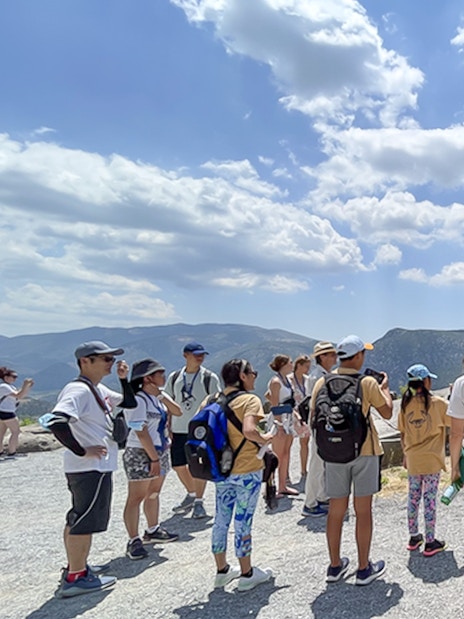 Visitors touring ancient ruins at Delphi, Greece, with guide explaining historical significance.