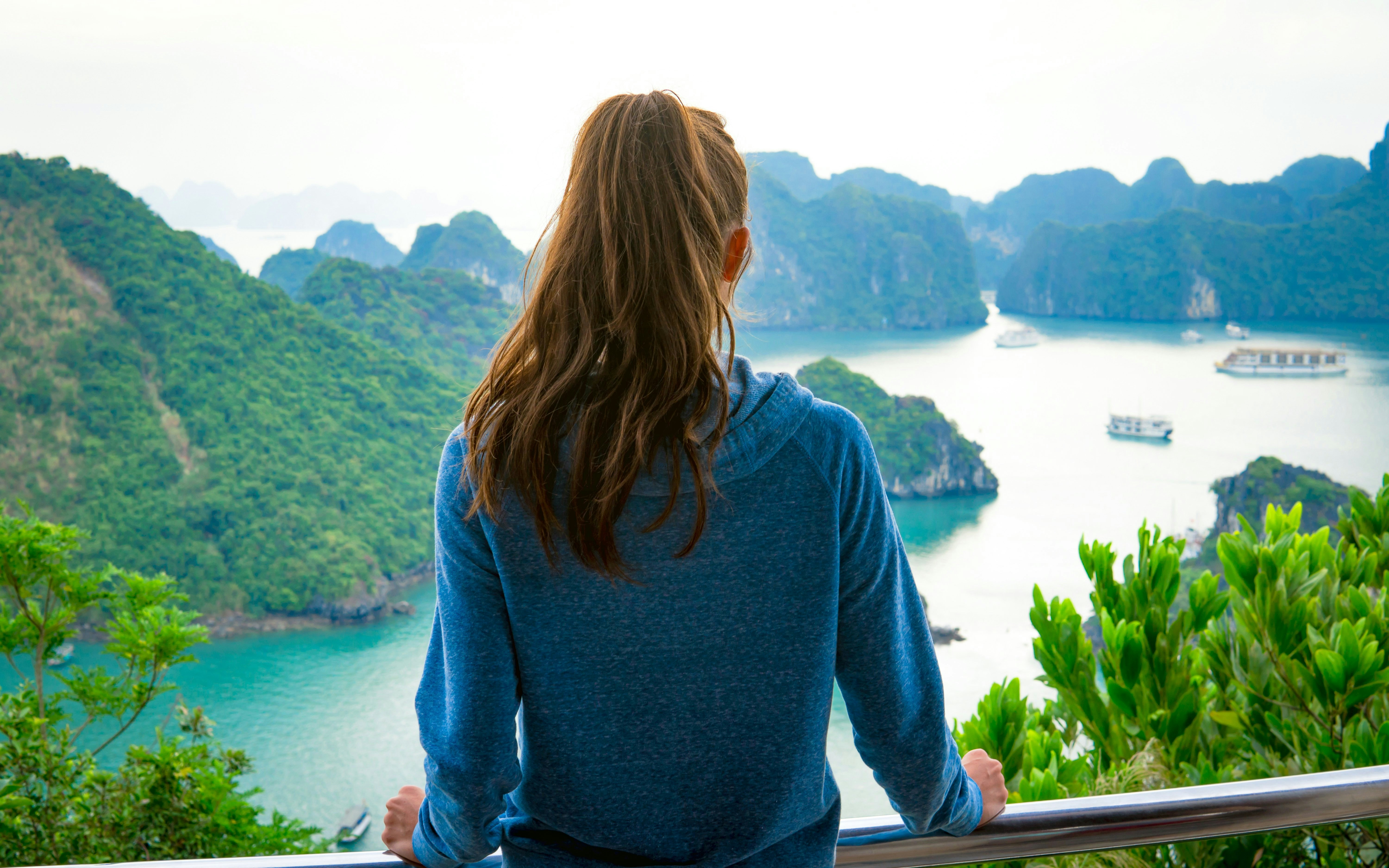 Woman overlooking Halong Bay from Ti Top Island, Vietnam, with limestone karsts and boats.