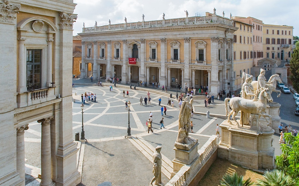Capitoline Museums and statues in Campidoglio Square, Rome, with visitors exploring.