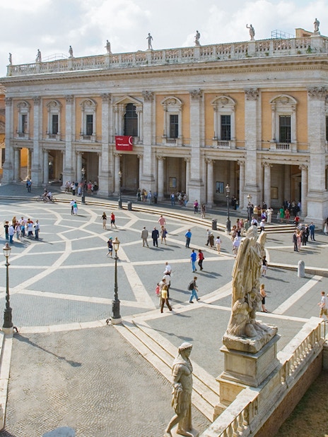 Capitoline Museums and statues in Campidoglio Square, Rome, with visitors exploring.