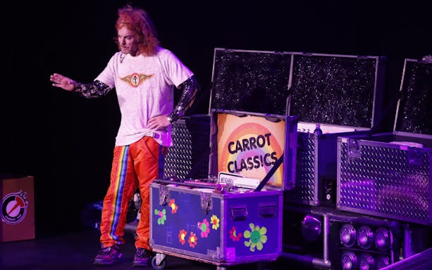 Performer on stage at Carrot Top show in Las Vegas with prop trunk labeled "Carrot Classics.