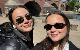 Two people smiling near the historic Alte Brücke bridge in Frankfurt, Germany.