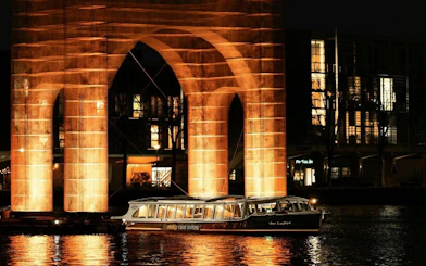 Canal cruise passing illuminated arch at Amsterdam Light Festival.