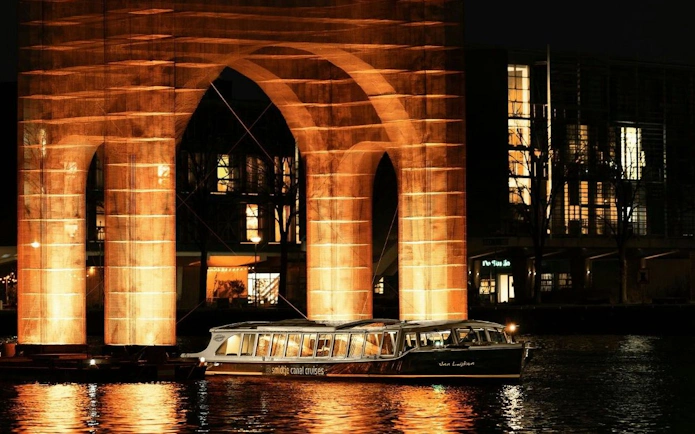 Canal cruise passing illuminated arch at Amsterdam Light Festival.