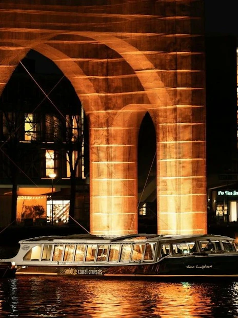 Canal cruise passing illuminated arch at Amsterdam Light Festival.