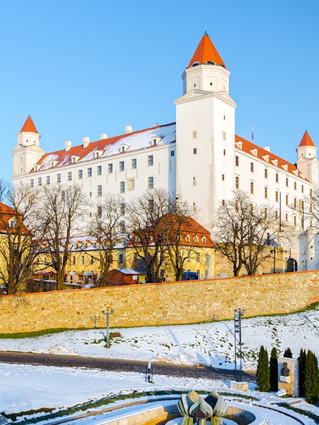Bratislava Castle in winter with snow-covered grounds and clear blue sky.