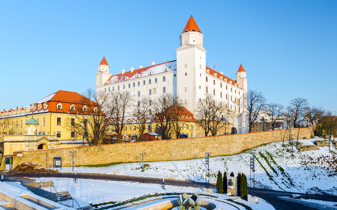 Bratislava Castle in winter with snow-covered grounds and clear blue sky.