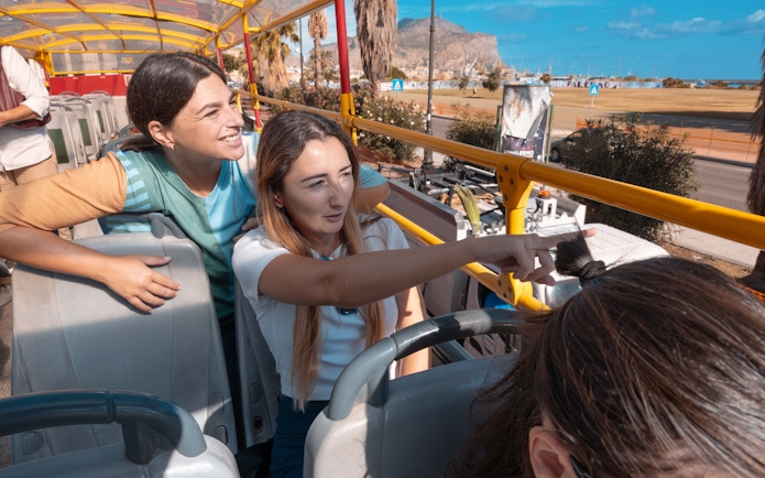 People enjoying a City Sightseeing bus tour in Palermo, pointing at landmarks.