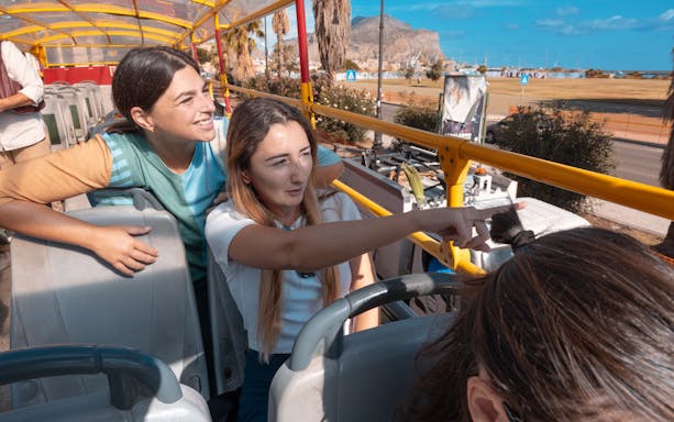People enjoying a City Sightseeing bus tour in Palermo, pointing at landmarks.