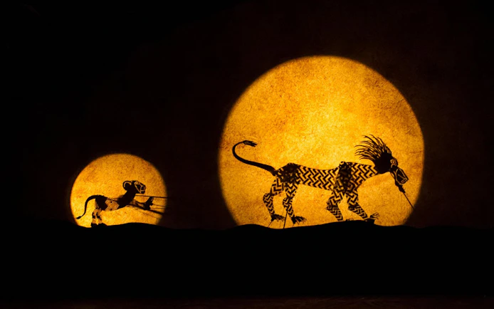Silhouettes of animals in "The Lion King" stage show against a glowing backdrop.