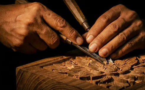 Hands carving intricate wood design at a workshop in Al Haouz, Marrakesh.