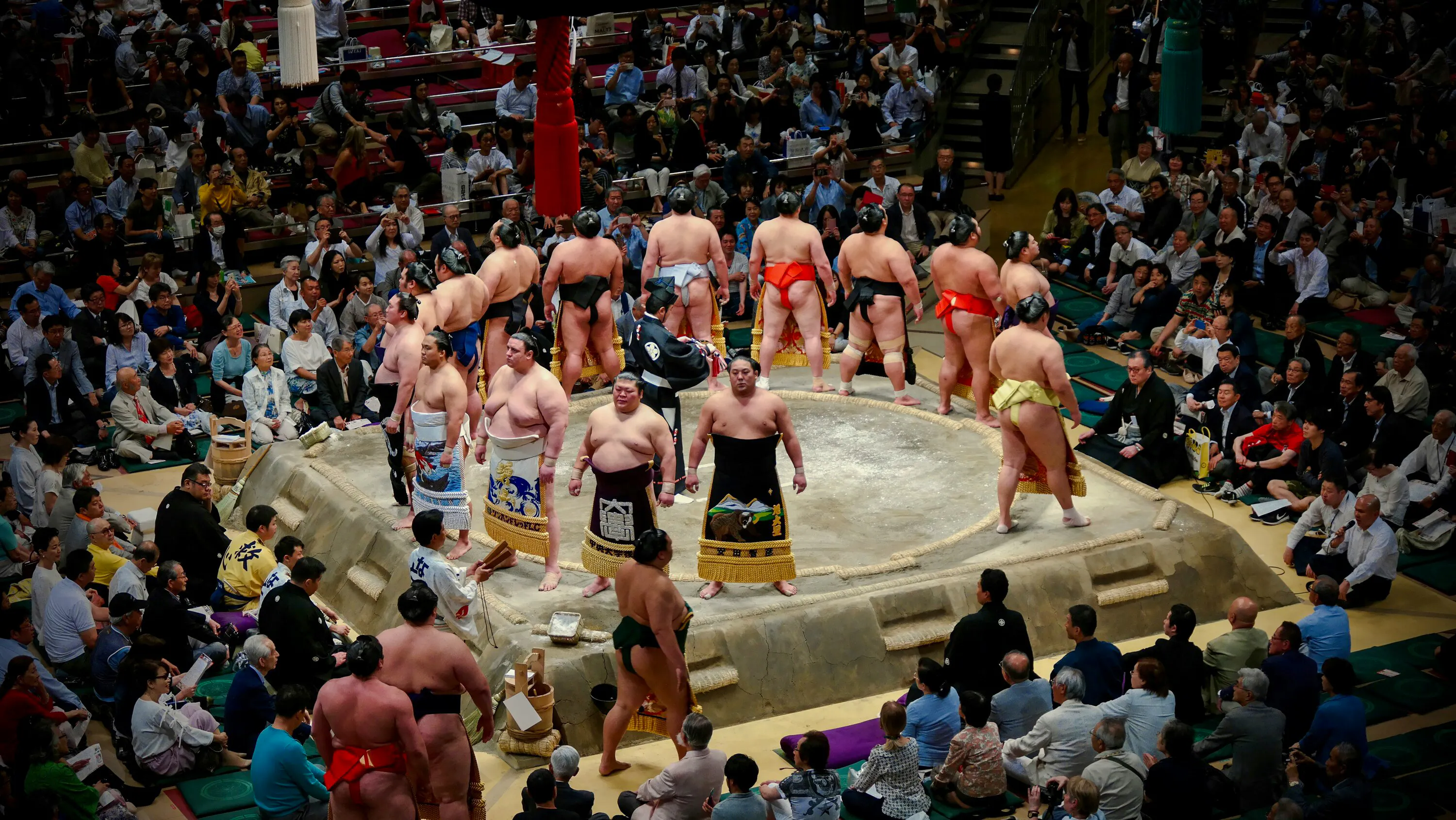 Sumo wrestlers in a ring during the Fukuoka Grand Sumo Tournament with spectators watching.