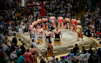 Sumo wrestlers in a ring during the Fukuoka Grand Sumo Tournament with spectators watching.