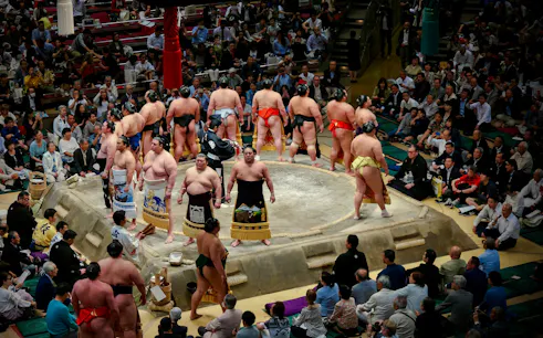 Sumo wrestlers in a ring during the Fukuoka Grand Sumo Tournament with spectators watching.