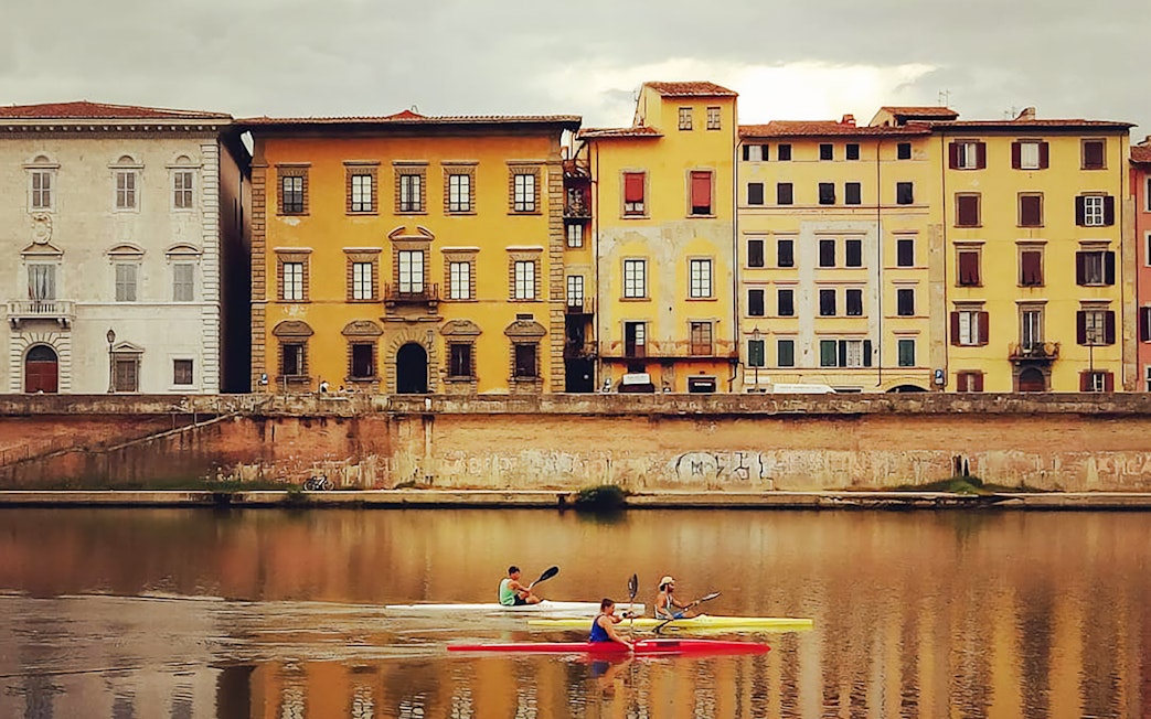 Kayakers on the Arno River with historic Pisa buildings in the background.