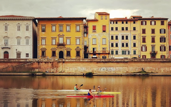 Kayakers on the Arno River with historic Pisa buildings in the background.