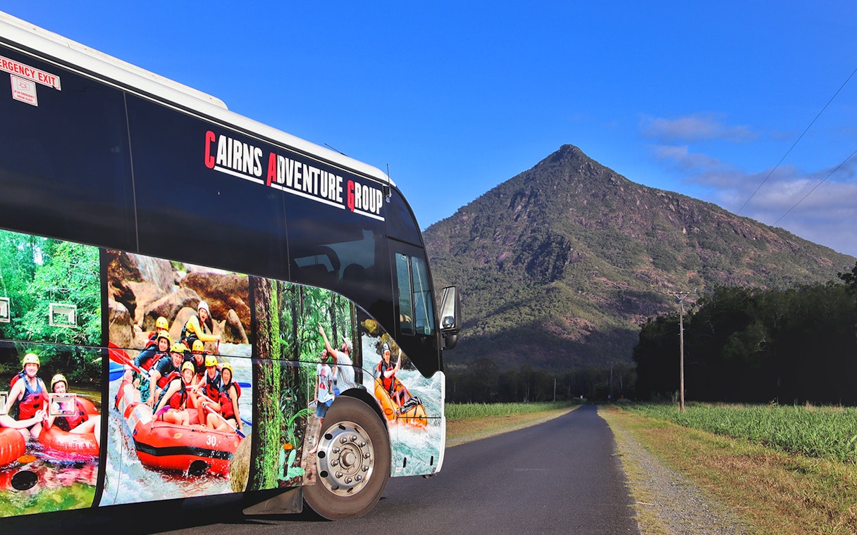 Tour bus on a road with a mountain backdrop in Queensland for Half-Day Waterfall Wanderers Tour.