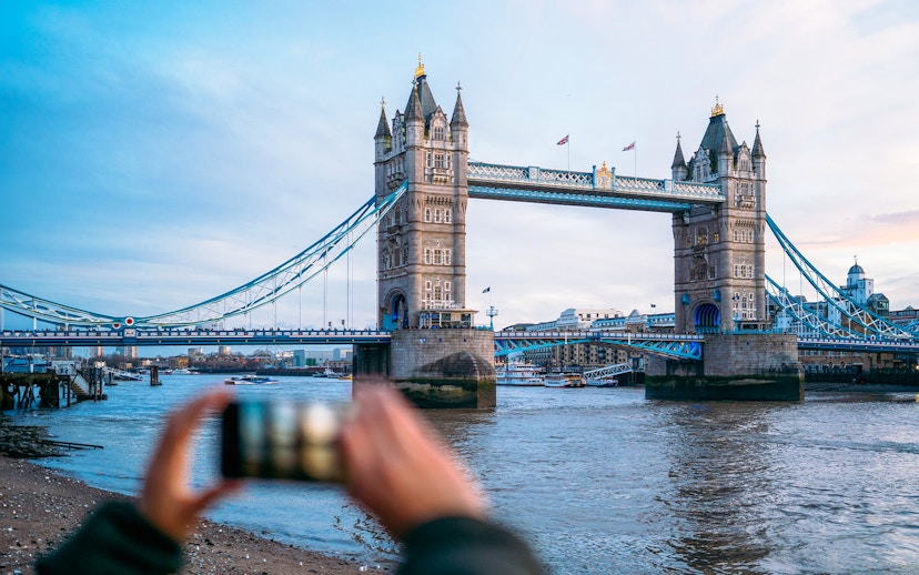 Tower Bridge in London with a person taking a photo, view from the riverbank.