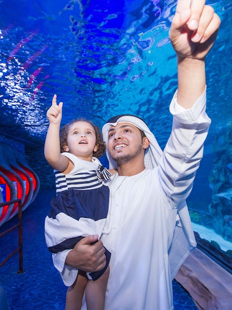 Father and child pointing at marine life in Dubai Aquarium tunnel.