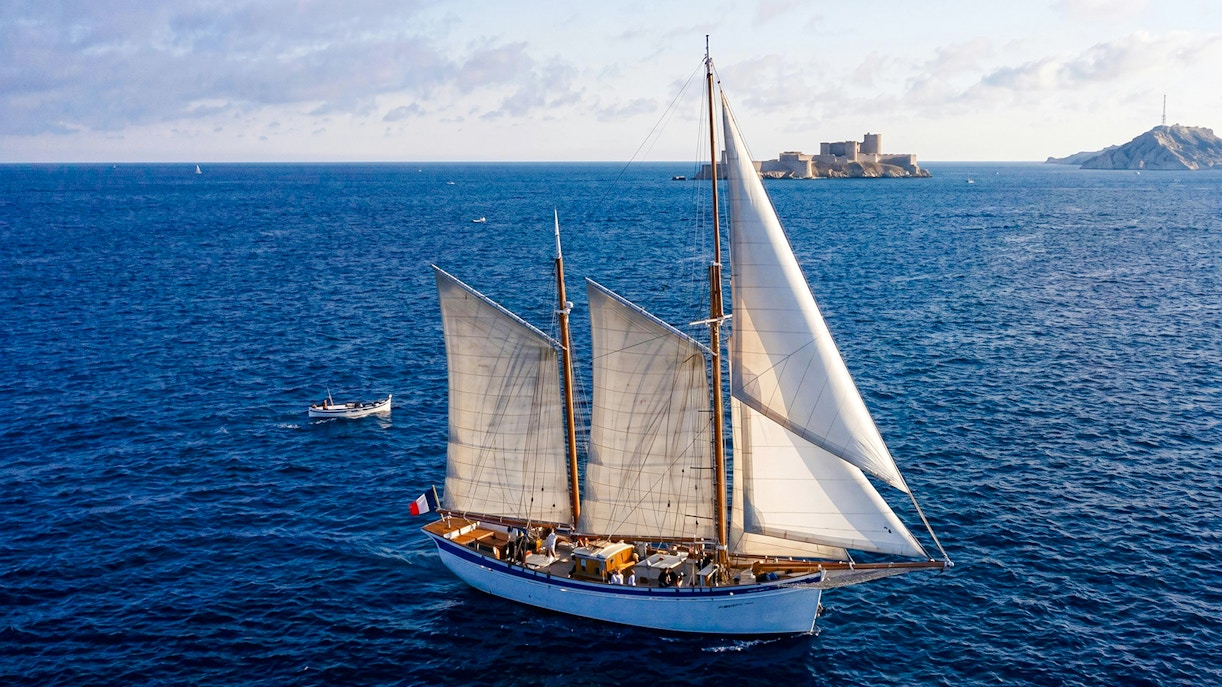 Sailing ship near Calanques with fortress in background, France.
