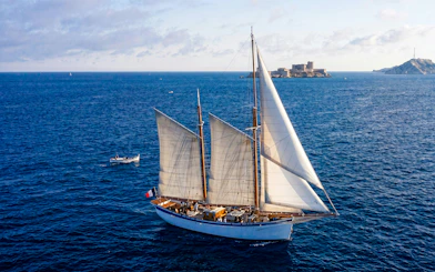Sailing ship near Calanques with fortress in background, France.