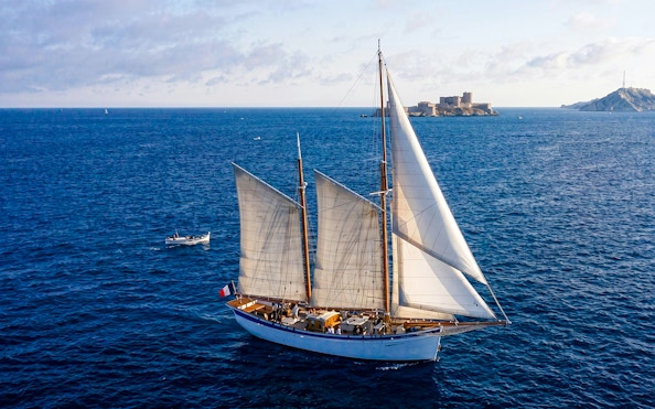 Sailing ship near Calanques with fortress in background, France.