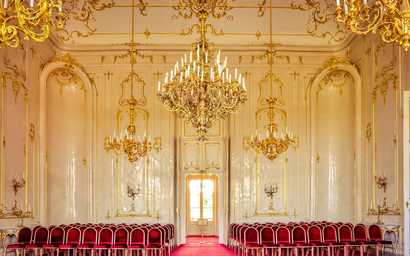 Royal Palace of Gödöllő interior with ornate chandeliers and red velvet chairs.