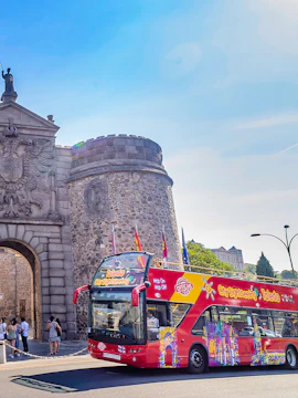 Open-top tour bus in front of Toledo's historic city gate.