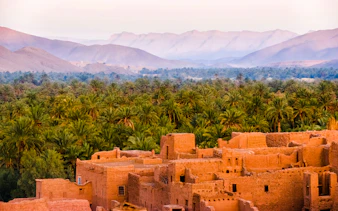 Ancient kasbah with palm grove and Atlas Mountains in Morocco.